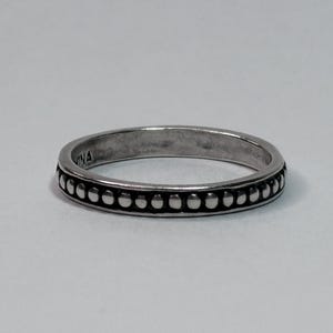 May include: A silver ring with a beaded design around the band. The ring has a simple, elegant style, with small, evenly spaced beads. The word "VINA" is engraved on the ring. This ring is a piece of jewelry.