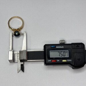 Puede incluir: Un anillo de oro con una piedra preciosa azul oscuro se mide con un calibrador digital. El calibrador muestra una medida de 7,50 mm. El anillo est&aacute; posicionado en las mordazas de medici&oacute;n del calibrador.