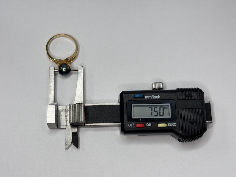 Puede incluir: Un anillo de oro con una piedra preciosa azul oscuro se mide con un calibrador digital. El calibrador muestra una medida de 7,50 mm. El anillo est&aacute; posicionado en las mordazas de medici&oacute;n del calibrador.