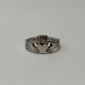 May include: A silver Claddagh ring featuring a heart, crown, and hands design. The ring's band has a decorative pattern. The Claddagh ring is a traditional Irish ring representing love, loyalty, and friendship.
