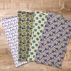 May include: Four fabric squares with different patterns. The first square is white with a repeating pattern of swords and shields. The second square is green with a repeating pattern of horses and shields. The third square is yellow with a repeating pattern of green leaves and a circle. The fourth square is gray with a repeating pattern of wizard hats and wands.