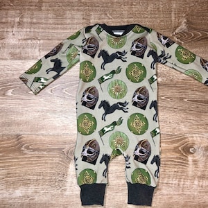 May include: A green and brown baby onesie with a repeating pattern of shields, horses, and helmets.