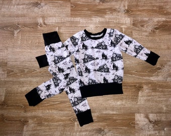 May include: Black and white pajamas with a train print. The pajamas feature a long-sleeved top and pants with a black waistband.