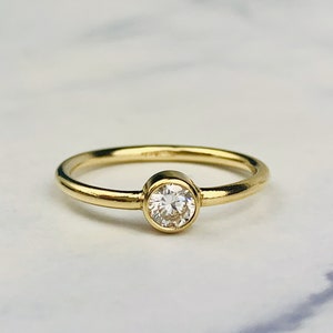 Op de afbeelding: Een eenvoudige gouden ring met een enkele ronde, bezel-gezet diamant.