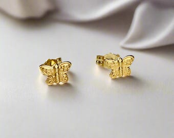 Puede incluir: Un par de pendientes de botón de mariposa de oro. Los pendientes son pequeños y delicados, con una superficie texturizada.