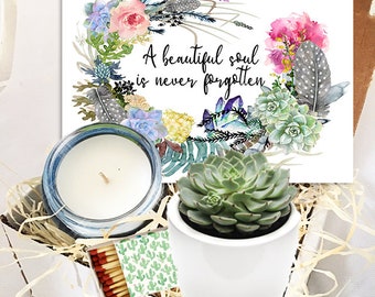 May include: A white gift box filled with a succulent plant in a white pot, a candle in a blue glass jar, and a box of matches. The box also includes a card with a watercolor floral wreath and the text "A beautiful soul is never forgotten."