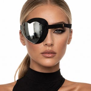 May include: Black eye patch with a heart-shaped mirrored lens. The patch is made of black fabric and has a strap to secure it around the head. The mirrored lens reflects the surrounding environment.