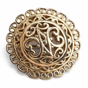 May include: A gold-colored vintage brooch with an ornate, openwork design. The brooch features a central circular element with an intricate pattern and a decorative outer edge. The overall style is classic and elegant.