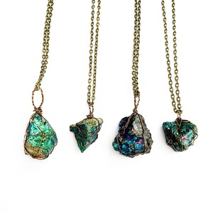 May include: Four necklaces with iridescent, teal-colored stones are displayed against a white background. Each stone is encased in a copper-colored wire cage and hangs from a matching chain. The necklaces vary slightly in stone shape and size.
