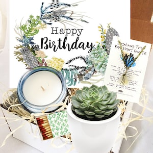 May include: A white gift box filled with a birthday gift set. The set includes a candle, a succulent plant in a white pot, a box of matches, and a necklace with a Joshua Tree quartz pendant. The box is decorated with a card that says "Happy Birthday" and a watercolor illustration of a wreath with feathers and succulents.