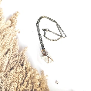 May include: A delicate gold chain necklace with a clear quartz crystal pendant wrapped in wire. The crystal is a natural, irregular shape.