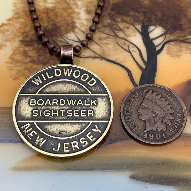 May include: A gold-toned necklace with a round pendant that reads "WILDWOOD BOARDWALK SIGHTSEER NEW JERSEY". The pendant is attached to a chain with small, round beads.