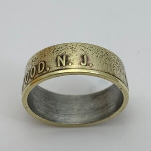 May include: A gold-toned ring with a textured surface and the inscription "WOOD. N. J." on the band.