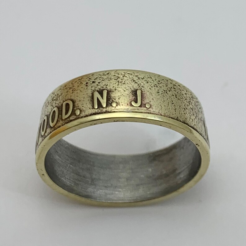 May include: A gold-toned ring with a textured surface and the inscription "WOOD. N. J." on the band.