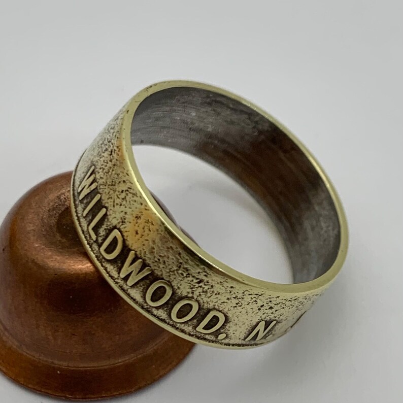 May include: A gold-toned ring made from a coin with the inscription "WILDWOOD, NJ" on the side.