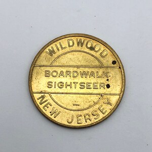 May include: A round, brass-colored token with the words "WILDWOOD BOARDWALK SIGHTSEER NEW JERSEY" embossed around the edges. The token has a slightly worn appearance, with small dark spots.