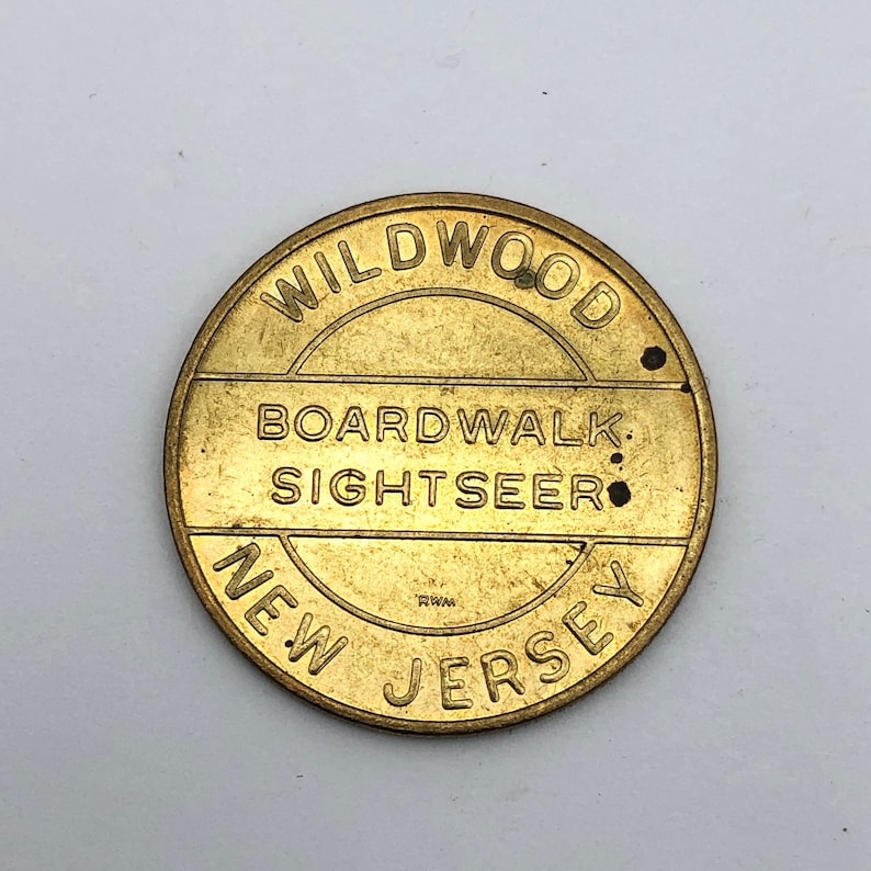 May include: A round, brass-colored token with the words "WILDWOOD BOARDWALK SIGHTSEER NEW JERSEY" embossed around the edges. The token has a slightly worn appearance, with small dark spots.