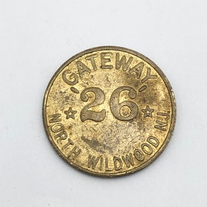May include: A round, aged brass token with the text "GATEWAY 26 NORTH WILDWOOD N.J." The number 26 is prominently displayed in the center, flanked by star shapes. The token has a worn, vintage appearance.
