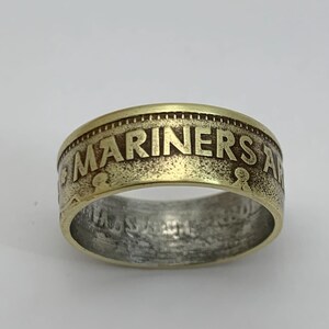 May include: A gold-toned ring made from a US Mariner's coin. The ring features the inscription "US MARINERS ARE" on the top.