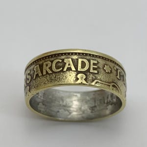 May include: A gold-toned ring made from a coin with the word "ARCADE" engraved on the band.