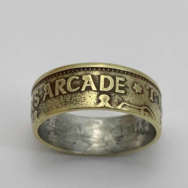 May include: A gold-toned ring made from a coin with the word "ARCADE" engraved on the band.