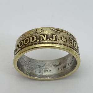 May include: A gold-toned ring made from a coin with the inscription "WOOD, N.J." on the band.