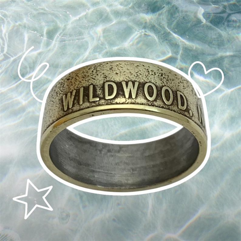 May include: A gold-colored metal ring with the words "WILDWOOD" engraved on the top. The ring is worn and has a distressed look.