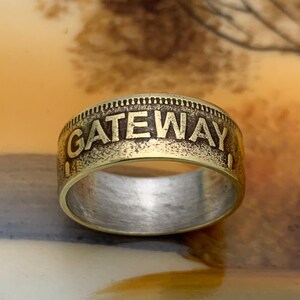 May include: A brass-toned ring with the word "GATEWAY" embossed around the band. The ring has a textured outer edge and a silver-colored interior. The ring is a piece of jewelry.