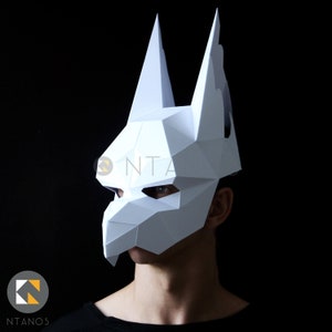 K&ouml;nnte beinhalten: Wei&szlig;e Papiermaske mit geometrischem Design, das an einen Wolfskopf erinnert. Die Maske hat spitze Ohren und eine scharfe Schnauze.