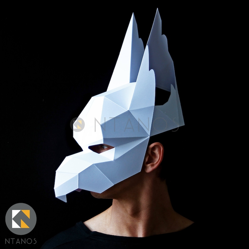 K&ouml;nnte beinhalten: Eine wei&szlig;e Papiermaske mit geometrischem Design, die an einen Wolfskopf oder einen Hundekopf erinnert. Die Maske hat gro&szlig;e, spitze Ohren und eine lange Schnauze.