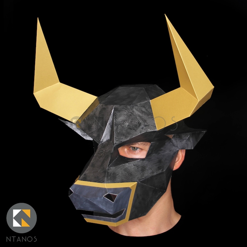 May include: A black and gold bull mask with a geometric design. The mask has a textured surface and is worn by a person.