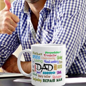 May include: White ceramic mug with a colorful word cloud design that reads "Father, Provider, Protector, Supportive, Understanding, Giving, Loving, Hard working, Fun, Dad, Fixer, Devoted, Kind, Smart, Hero, Strong, Ever, Reliable, Comforting, Repair Man".