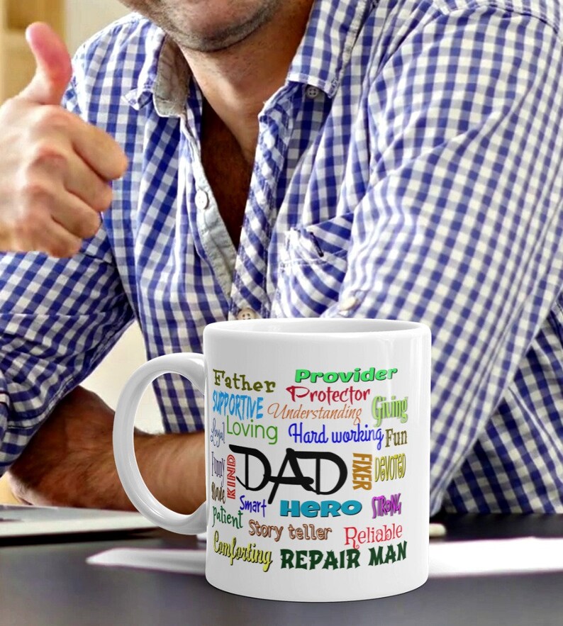 May include: White ceramic mug with a colorful word cloud design that reads "Father, Provider, Protector, Supportive, Understanding, Giving, Loving, Hard working, Fun, Dad, Fixer, Devoted, Kind, Smart, Hero, Strong, Ever, Reliable, Comforting, Repair Man".