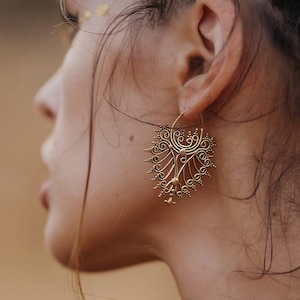 May include: A side profile shows gold-coloured filigree earrings with a leaf-like design. The earrings feature intricate swirls and small dangling details. A multi-strand gold beaded necklace is also visible.
