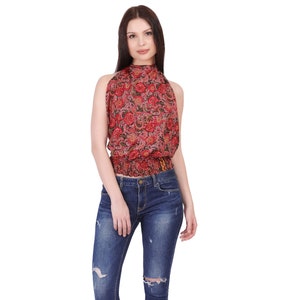 Op de afbeelding: Een vrouw draagt een rode paisley haltertop en een distressed blauwe jeans. De top heeft een hoge halslijn en een gerimpelde taille. De jeans heeft gescheurde knieën en een slanke pasvorm. Zwarte open-teen hakken maken de outfit compleet.