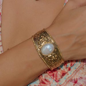 May include: Gold-coloured jewellery set including a pendant necklace, earrings, a bracelet, and a ring. The pendant necklace has an oval locket with a central stone. The bracelet has a large central stone. The earrings are hoop-shaped.