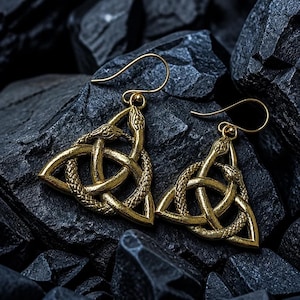Peut inclure: Une paire de boucles d'oreilles pendantes dorées présentant un motif de nœud triquetra formé par des serpents entrelacés aux écailles texturées. Chaque boucle est suspendue à un crochet simple, avec une finition métallique détaillée.