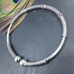 May include: Silver-toned bangle bracelet with a coiled wire design and decorative accents. The bracelet features two silver spheres and is set against a dark background. The bracelet is a piece of jewelry.