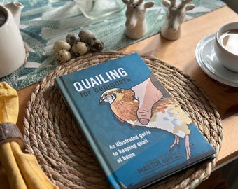 May include: A blue book titled "Quailing for beginners" with an illustration of a quail being held in a hand. The book is on a woven straw placemat with quail eggs in the background.