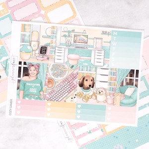 May include: A sticker sheet titled COZY GAMER featuring illustrations of a gaming desk, a person in a green shirt with the text SWITCHING TO COZY MODE, a keyboard, a bowl of cereal, a dachshund, and a cozy room with a teal armchair and shelves.