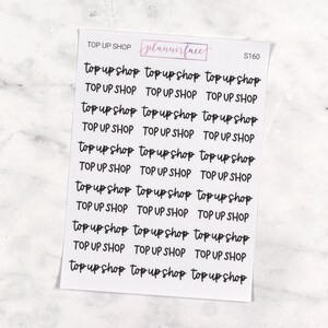May include: A sheet of stickers with the text "top up shop" repeated multiple times in a handwritten font. The stickers are designed for use in a planner or journal.