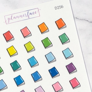 May include: A sheet of colorful book stickers with a rainbow of colors, including red, orange, yellow, green, blue, purple, and pink. The stickers are all the same size and shape, and they feature a simple design of a closed book. The sheet is labeled "D256" and "plannerface".