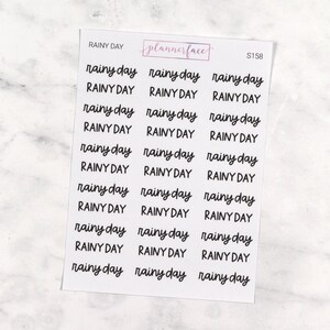May include: A white sheet of planner stickers featuring the words "rainy day" in a handwritten style, repeated across the sheet. The brand name "plannerface" is in a pink box at the top. The code S158 is also visible.