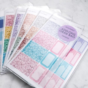 Puede incluir: Una colección de pegatinas para planificador en varios colores, incluyendo rosa, azul, verde y dorado, con detalles de purpurina. Las pegatinas están empaquetadas en plástico transparente y etiquetadas con frases como "Love is Love".