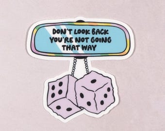 May include: A sticker featuring a blue rearview mirror with the text "Don't look back you're not going that way" and two purple dice hanging from it.