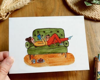 Może przedstawiać: Ręcznie rysowana ilustracja przedstawiająca osobę czytającą na zielonej sofie. Osoba ma na sobie żółtą górę i czerwone spodnie. Kot spoczywa na jej piersi. Mały stolik z kubkiem i ciastem. Grafika jest na białym papierze.