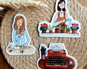 Może przedstawiać: Zestaw trzech naklejek wyciętych z ilustracjami kobiety czytającej książkę z kotem, kobiety podlewającej rośliny i zabytkowej maszyny do pisania z filiżanką kawy. Naklejki mają białą obwódkę.
