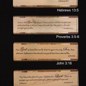 May include: Four wooden plaques with Bible verses. Each plaque has a light wood grain with a decorative border. The verses include Hebrews 13:5, Proverbs 3:5-6, John 3:16, and Jeremiah 29:11. The text is in a dark font.