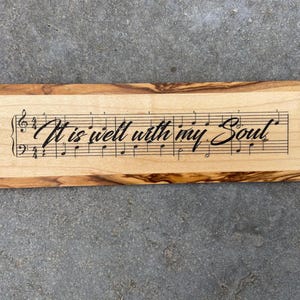 May include: A wooden cutting board with the words "It is well with my Soul" engraved on it. The words are set against a musical staff with notes.