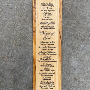 May include: A wooden bookmark with the names of God in Hebrew and English. The bookmark is engraved with the words "Names of God" and lists various names of God, such as "El Shaddai", "El Elyon", "Adonai", "Yahweh", "Jehovah Nissi", "Jehovah Raah", "Jehovah Rapha", "Jehovah Shammah", "Jehovah Tsidkenu", "Jehovah Mekoddishkem", "El Olam", "Elohim", "Jehovah Sabaoth", "Quanna", "Jehovah Jireh", and "Jehovah Shalom".